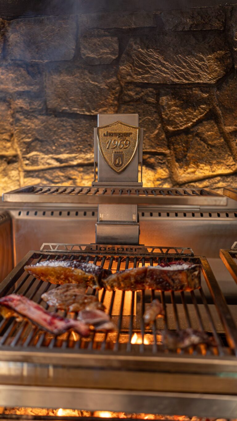The Basque grill with meat over the embers, under the Josper crest