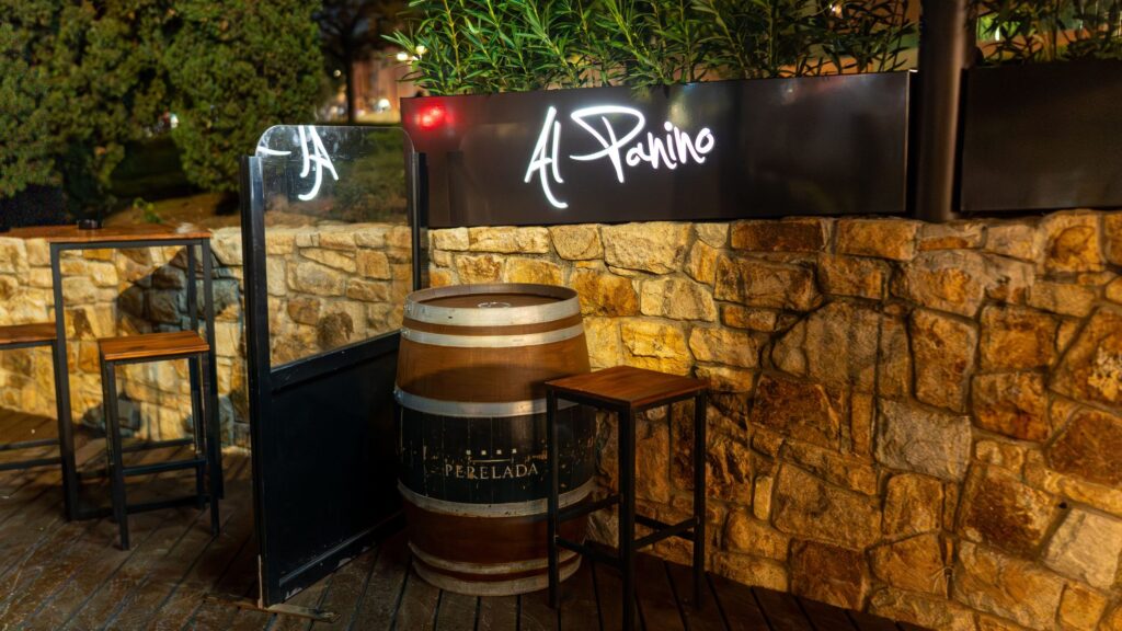 A corner of the terrace with a barrel and high tables by the stone wall